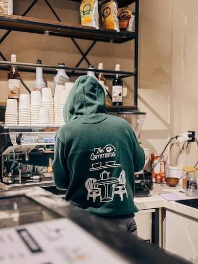 Barista in a The Commons Coffee hoodie preparing drinks behind the counter in Abbottabad