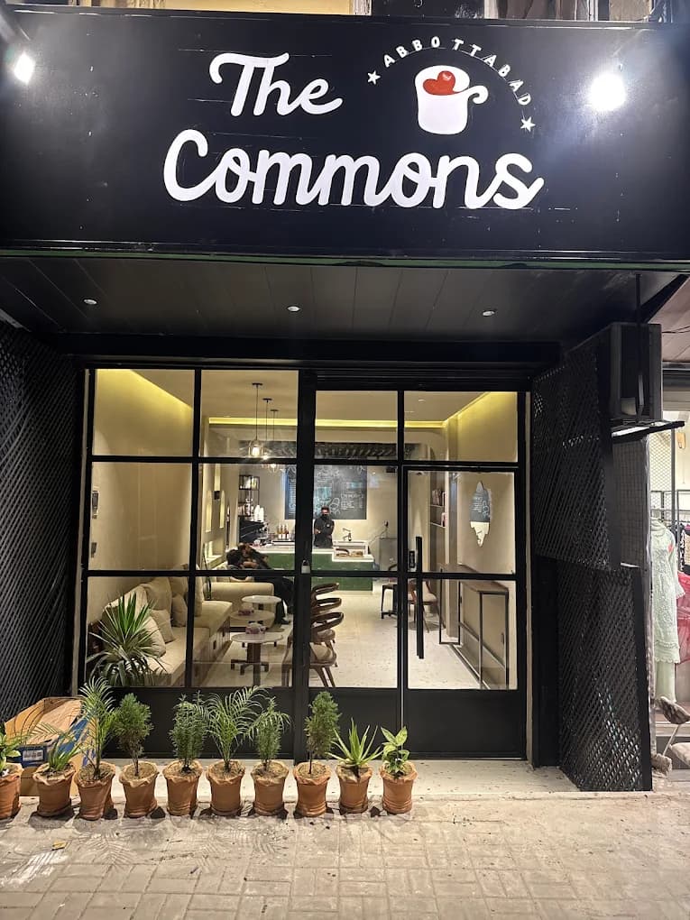 The Commons Coffee storefront entrance at night with potted plants, Abbottabad