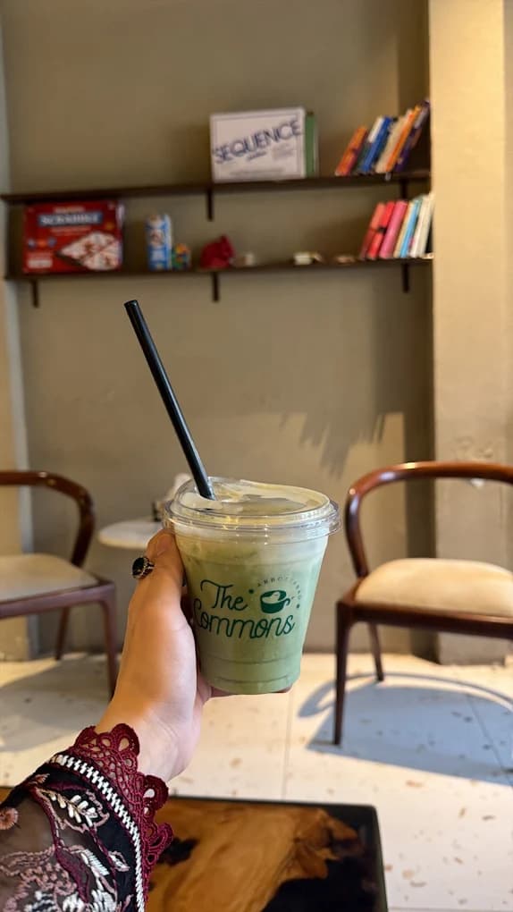 Hand holding an iced matcha in a The Commons Coffee branded cup