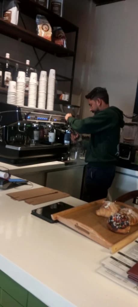 Barista preparing an espresso drink with fresh croissants and donuts on the counter